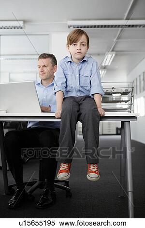 Stock Photography - Boy sitting on desk with businessman working. Fotosearch