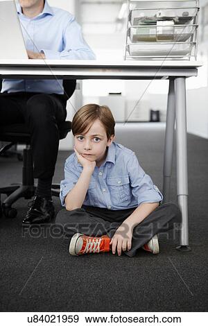 Boy sitting on floor with businessman working at desk View Large Photo Image Stock Photo - Boy sitting on floor with businessman working at desk. Fotosearch
