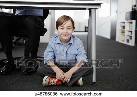 Stock Photograph - Boy sitting on floor with businessman working at desk. Fotosearch