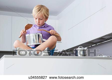 Boy sitting on kitchen counter playing drums with pans and wooden spoons View Large Photo Image Stock Photo - Boy sitting on kitchen counter playing drums with pans and wooden spoons. Fotosearch