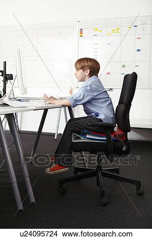 Boy sitting on ring binders on office chair using computer View Large Photo Image Picture - Boy sitting on ring binders on office chair using computer. Fotosearch