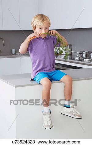 Boy sitting on side in kitchen with carrot moustache View Large Photo Image Stock Image - Boy sitting on side in kitchen with carrot moustache. Fotosearch