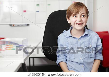 Boy wearing blue shirt on office chair View Large Photo Image Picture - Boy wearing blue shirt on office chair. Fotosearch