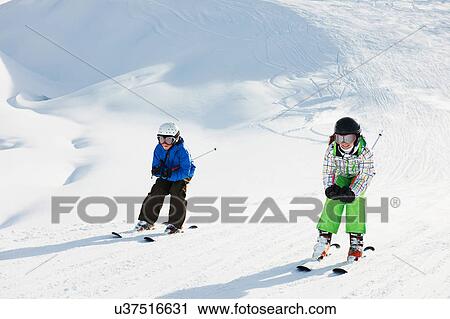 Stock Image - Brother and sister skiing, Les Arcs, Haute-Savoie, France. Fotosearch