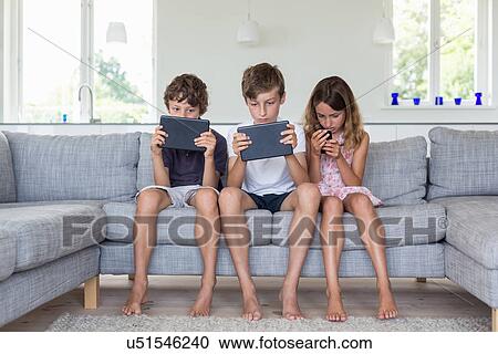 Brothers and sister on sofa with digital tablets and mobile View Large Photo Image Stock Image - Brothers and sister on sofa with digital tablets and mobile. Fotosearch