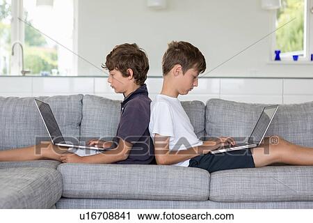 Brothers back to back on sofa using computers View Large Photo Image Stock Image - Brothers back to back on sofa using computers. Fotosearch
