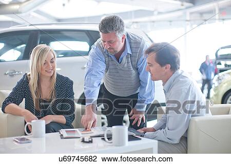 Stock Image - Car salesman advising couple in car showroom. Fotosearch