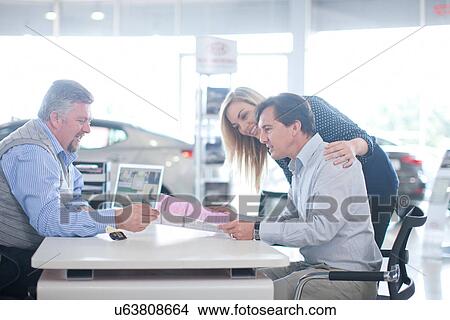 Car salesman and couple looking at contract in showroom View Large Photo Image Picture - Car salesman and couple looking at contract in showroom. Fotosearch