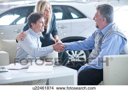 Car salesman and couple shaking hands in car showroom View Large Photo Image Picture - Car salesman and couple shaking hands in car showroom. Fotosearch