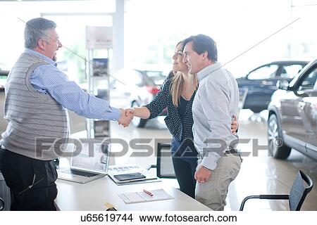Car salesman and couple shaking hands in car showroom View Large Photo Image Picture - Car salesman and couple shaking hands in car showroom. Fotosearch
