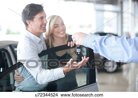 Car salesman handing key to couple in showroom View Large Photo Image Picture - Car salesman handing key to couple in showroom. Fotosearch