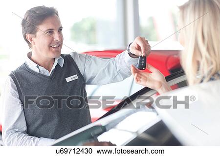 Car salesman handing keys to young woman in showroom View Large Photo Image Stock Image - Car salesman handing keys to young woman in showroom. Fotosearch