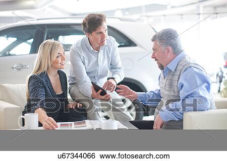 Car salesman talking to couple in car showroom View Large Photo Image Stock Photograph - Car salesman talking to couple in car showroom. Fotosearch