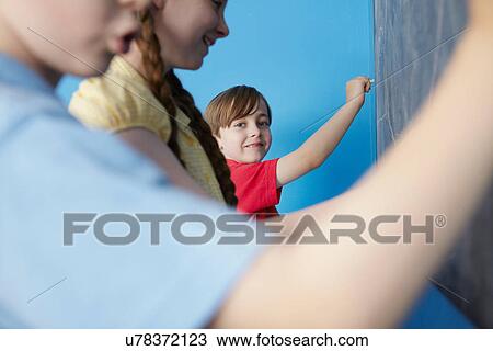 Stock Image - Children writing on blackboard, blue background. Fotosearch
