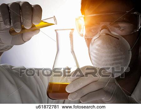 Stock Image - Close up of scientist pouring liquid into flask. Fotosearch