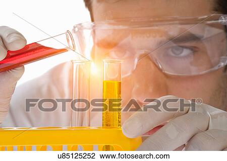 Stock Image - Close up of scientist pouring liquid into test tube. Fotosearch