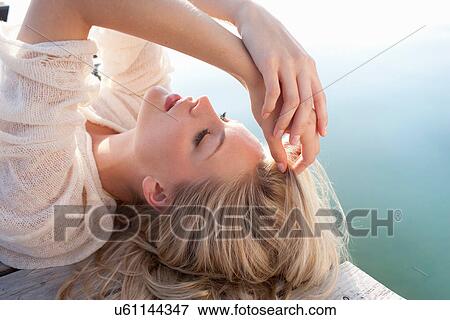 Stock Photo - Close up of young woman lying on lake pier. Fotosearch