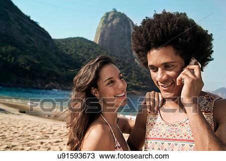 Stock Image - Couple on beach, man on cell phone, Rio de Janeiro, Brazil. Fotosearch