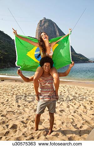 Stock Image - Couple on beach with Brazilian flag, Rio de Janeiro, Brazil. Fotosearch