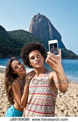 Couple photographing themselves on beach with camera phone, Rio de Janeiro, Brazil View Large Photo Image Stock Photograph - Couple photographing themselves on beach with camera phone, Rio de Janeiro, Brazil. Fotosearch
