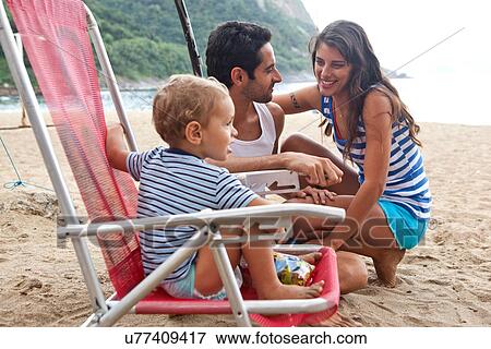 Stock Photo - Family on beach, boy sitting on chair. Fotosearch