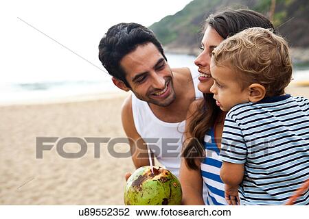 Stock Image - Family on beach with coconut drink. Fotosearch