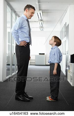 Stock Image - Father and son standing face to face in office. Fotosearch
