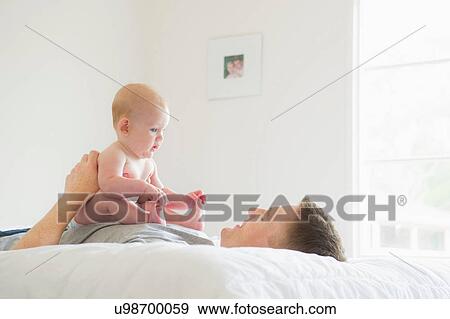 Stock Photo - Father lying on bed holding baby. Fotosearch
