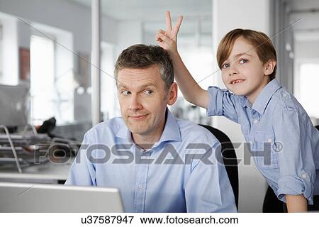 Father using laptop, son making peace sign behind his head View Large Photo Image Stock Photo - Father using laptop, son making peace sign behind his head. Fotosearch
