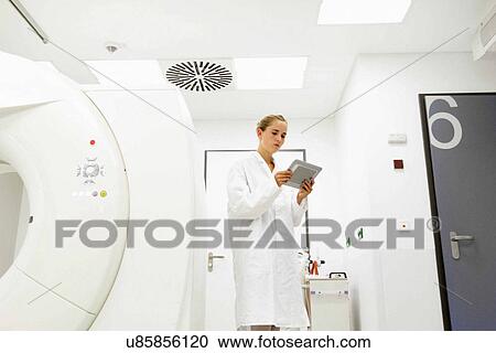 Stock Image - Female doctor looking at digital tablet in treatment room. Fotosearch