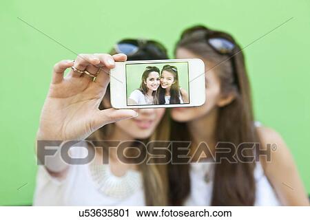 Stock Image - Female friends taking a picture of themselves with smartphone. Fotosearch