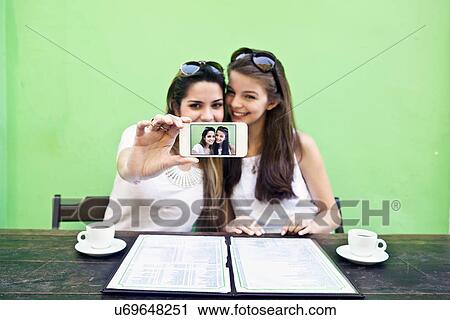 Female friends taking a picture of themselves with smartphone at cafe View Large Photo Image Stock Image - Female friends taking a picture of themselves with smartphone at cafe. Fotosearch