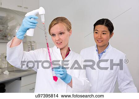 Picture - Female scientists at work in laboratory, pipetting liquid for reaction mixture. Fotosearch