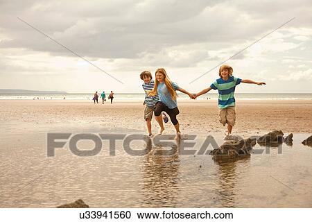 Stock Image - Friends running on beach, Devon, England, UK. Fotosearch