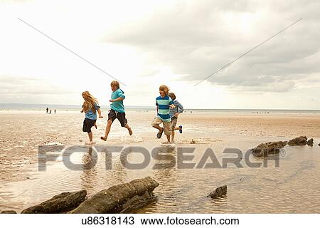Stock Image - Friends running on beach, Devon, England, UK. Fotosearch
