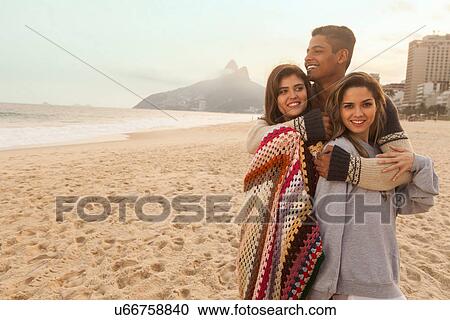 Stock Image - Friends wrapped in blanket, Ipanema Beach, Rio de Janeiro, Brazil. Fotosearch