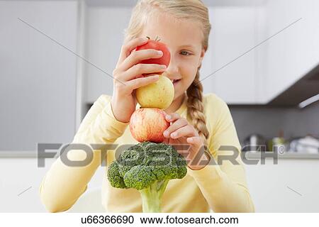 Stock Image - Girl building tower of apples and broccoli. Fotosearch