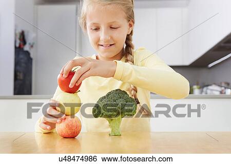 Stock Photograph - Girl building tower of apples and broccoli. Fotosearch