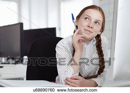 Stock Image - Girl holding biro and looking up in office. Fotosearch