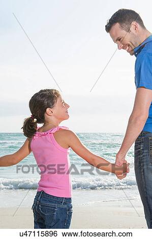 Girl holding hands with father at beach View Large Photo Image Stock Photograph - Girl holding hands with father at beach. Fotosearch