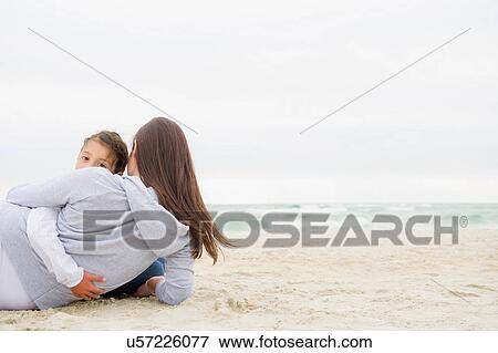 Stock Photo - Girl lying on beach with arm around mother. Fotosearch