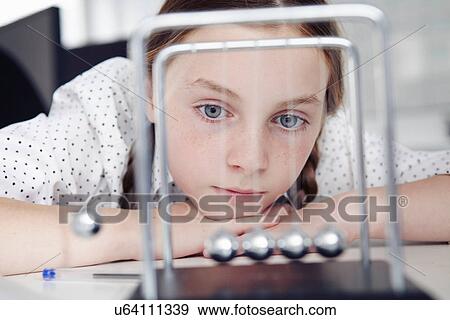 Girl playing with newton's cradle on desk View Large Photo Image Stock Photo - Girl playing with newton's cradle on desk. Fotosearch