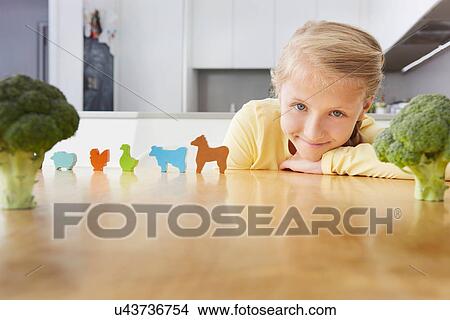 Picture - Girl playing with toy animals around broccoli. Fotosearch
