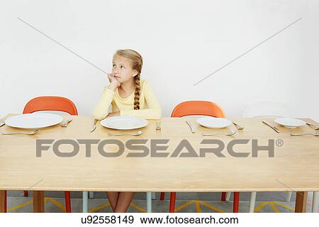 Stock Photo - Girl sitting at table with empty plate, looking away. Fotosearch