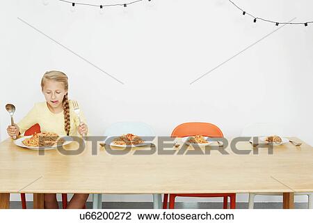 Stock Image - Girl sitting at table with spaghetti and three more plates. Fotosearch