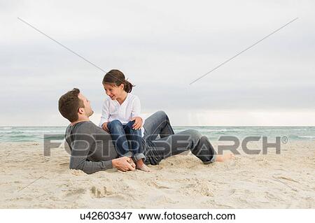 Girl sitting on father on beach View Large Photo Image Stock Photo - Girl sitting on father on beach. Fotosearch