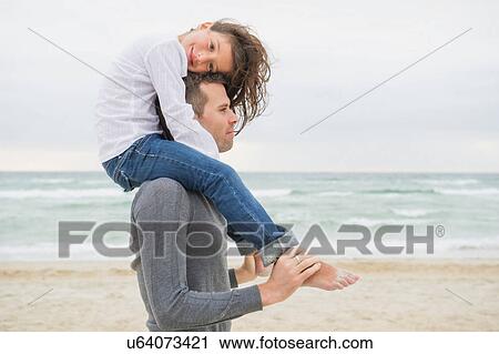 Girl sitting on father's shoulders on beach View Large Photo Image Stock Image - Girl sitting on father's shoulders on beach. Fotosearch