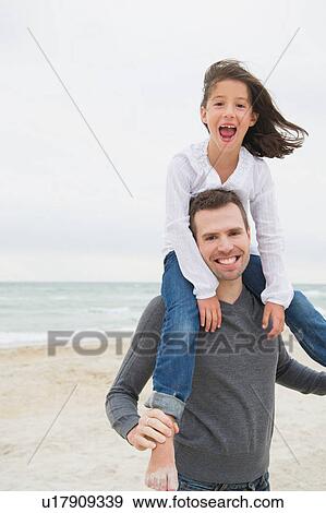 Girl sitting on father's shoulders on beach View Large Photo Image Stock Photo - Girl sitting on father's shoulders on beach. Fotosearch