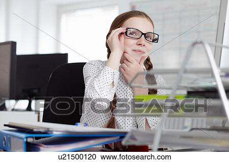 Girl wearing glasses with hand on chin in office View Large Photo Image Stock Image - Girl wearing glasses with hand on chin in office. Fotosearch