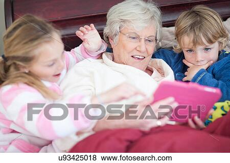 Stock Photo - Grandmother and grandchildren playing digital game in bed. Fotosearch